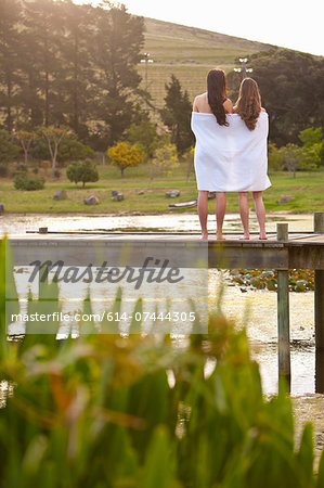 Two young women standing on river pier wrapped in blanket