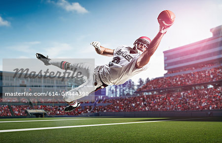 American football player catching ball mid air in stadium