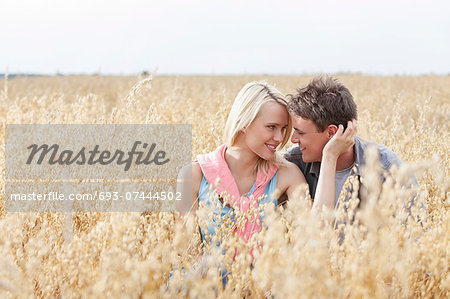 Romantic young couple looking at each other while relaxing amidst field