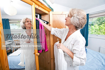 Senior woman selecting dress from closet at home