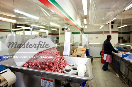 Minced meat in container with employee standing in background at store