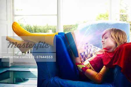 Little boy dressed as a super hero reading a book