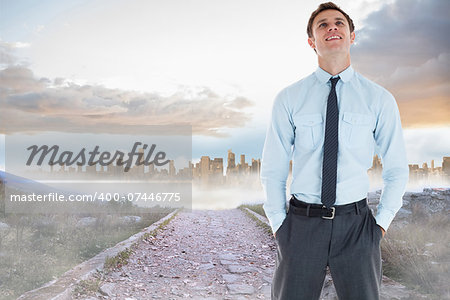 Smiling businessman standing with hand in pocket against rocky path leading to large urban sprawl