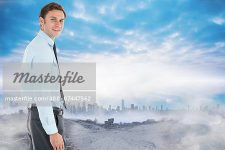 Happy businessman standing with hand in pocket against dusty path leading to city under the clouds