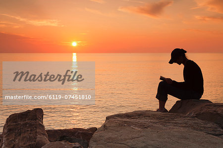 Woman sitting on the coast at sunset, reading, Corsica, France, Mediterranean, Europe