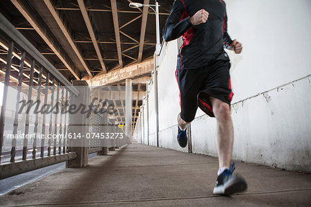Cropped shot of young man running on city bridge Cropped shot of young man running on city bridge