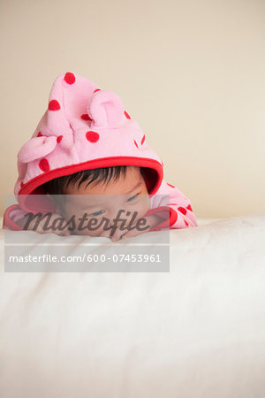 Portrait of two week old, newborn Asian baby girl in pink polka dot hooded jacket, studio shot on white background