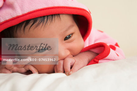 Close-up portrait of two week old Asian baby girl in pink polka dot hooded jacket, studio shot