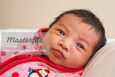 Close-up portrait of two week old Asian baby girl in pink polka dot jacket, studio shot