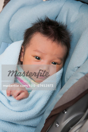 Close-up portrait of swaddled two week old, newborn Asian baby girl, lying in car seat