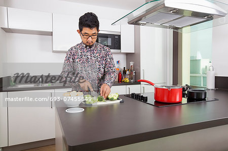 Young man cutting broccoli at kitchen counter