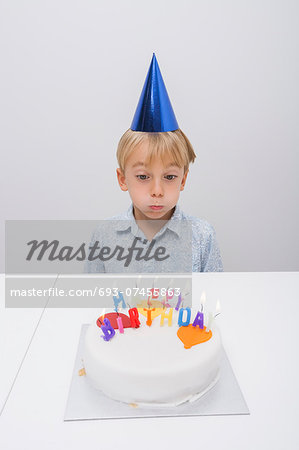 Boy blowing candles on birthday cake at table in house