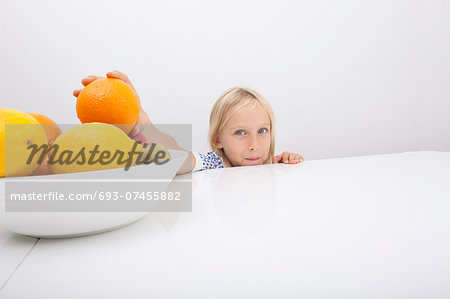 Portrait of little girl holding orange from fruit bowl