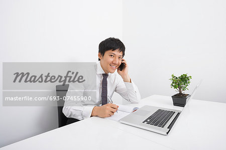 Portrait of happy businessman using cell phone while working at office desk