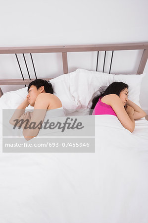 Unhappy Asian couple sleeping back to back in bed