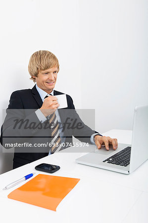Confident businessman having coffee white using laptop in office