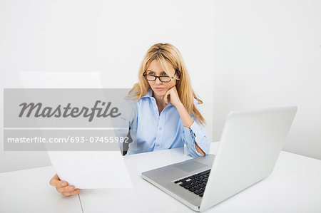 Businesswoman in eyeglasses reading document at office desk