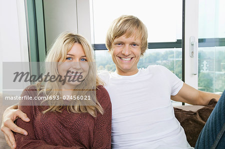 Portrait of cheerful couple sitting on sofa at home