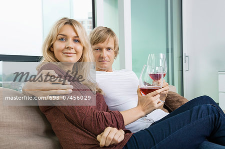 Portrait of smiling couple with wine glasses in living room at home