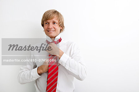 Portrait of mid adult businessman tying tie against white background