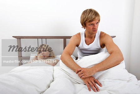 Angry man sitting on bed with woman in house