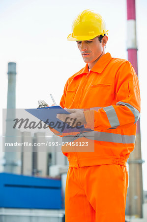 Male architect in protective workwear writing on clipboard at site