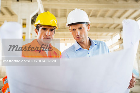 Male architects reviewing blueprint at construction site Male architects reviewing blueprint at construction site