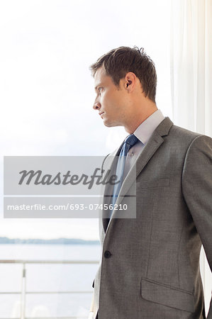 Pensive businessman standing by glass door in hotel