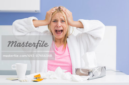 Portrait of young exhausted woman screaming while suffering from headache and cold in kitchen Portrait of young exhausted woman screaming while suffering from headache and cold in kitchen