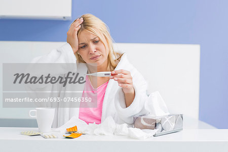 Young woman suffering from cold checking tempereature