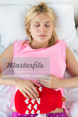 Young woman using hot water bottle on abdomen while lying on bed