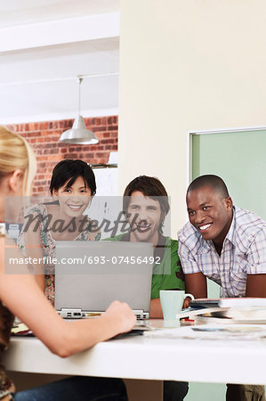 Four people having meeting around laptop laughing.