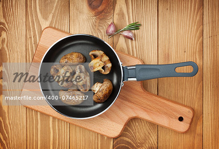 Fried mushrooms on frying pan over wooden table background