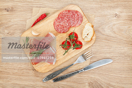 Prosciutto, salami, bread, vegetables and spices. Over wooden table background