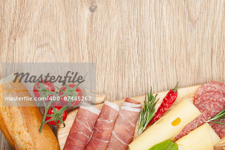 Cheese, prosciutto, bread, vegetables and spices. Over wooden table background with copy space
