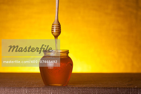 Honey jar with wooden dipper and flowing honey, studio shot