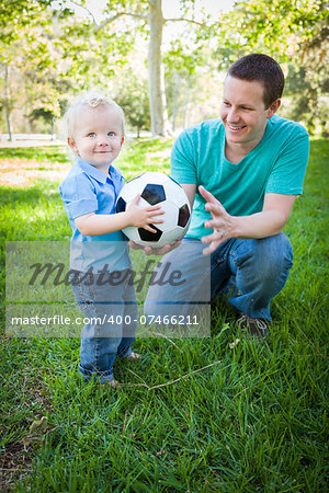 Young Cute Boy and Dad Playing with Soccer Ball in the Park.