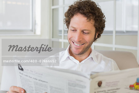 Closeup of a smiling young man reading newspaper on sofa in the house