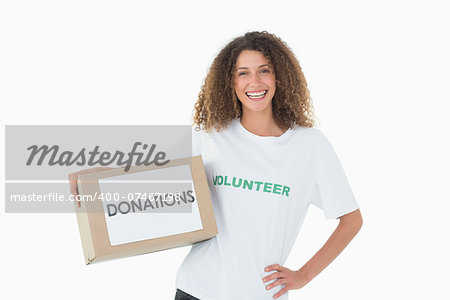 Smiling volunteer holding a box of donations with hand on hip on white background