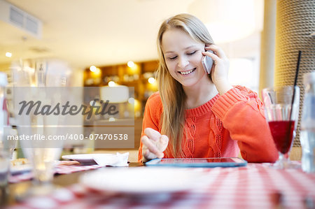 Young woman in cafe using her touchpad and answering phone call