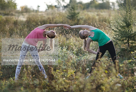 Two supple athletic young women working out together in the countryside doing bending and stretching exercises