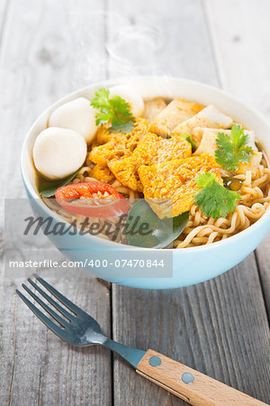 Spicy curry instant noodles soup with fork on wooden dining table. Fresh cooked, hot with steamed smoke.