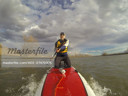 mature male paddler in wetsuit and life jacket enjoying workout on a stand up paddleboard (SUP), windy lake in one of nature areas in Fort Collins, Colorado,  distorted wide angle view