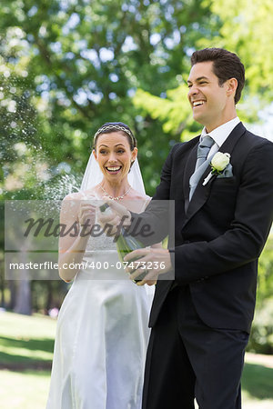 Young newlywed couple popping cork of champagne in park