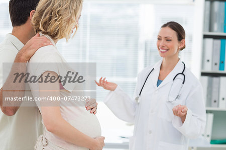 Beautiful female gynaecologist welcoming expectant couple in clinic