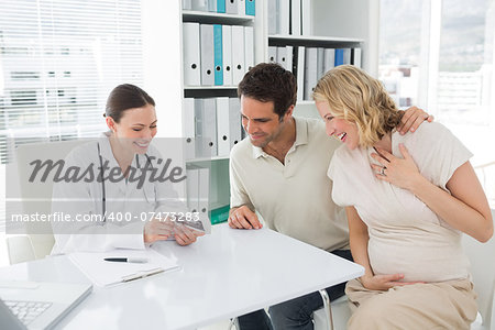 Happy female gynaecologist and expectant couple looking at sonography reports in clinic