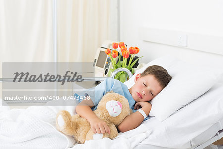 Sick little boy sleeping with teddy bear in hospital bed