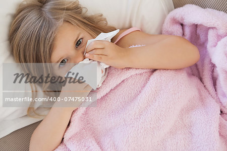 High angle portrait of a cute little girl suffering from cold as she lies in bed