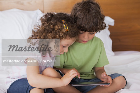 Young boy and girl using digital tablet in bed at home