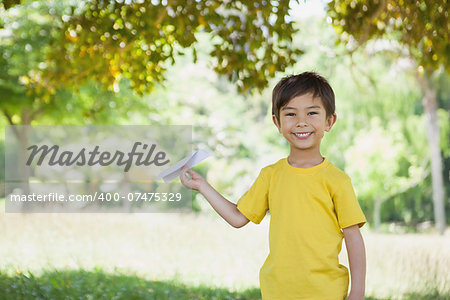 Portrait of a happy young boy playing with a paper plane at the park